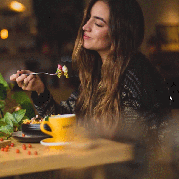 A young and smiling women sitting at a table and eats.